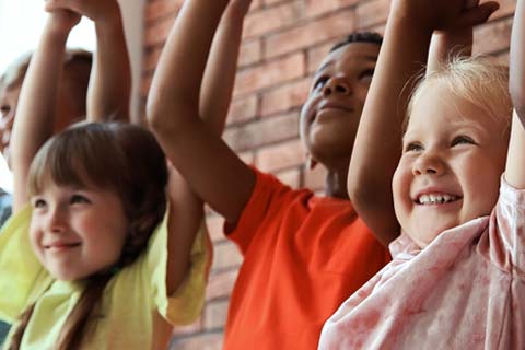 A group of childen standing together holding hands raised in the air.