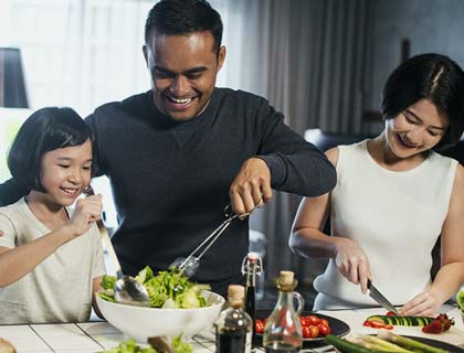 Father, mother, and daughter making a salad in their home.