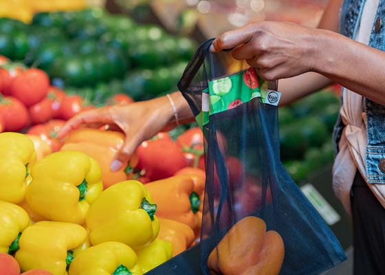 Person placing orange peppers in a reusable produce bag in a grocery store.
