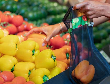Person placing orange peppers in a reusable produce bag in a grocery store.